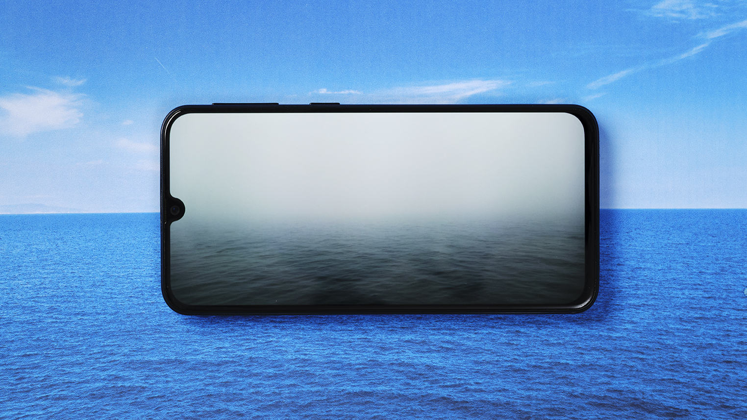 A foggy sea on a mobile phone screen over the image of a clear ocean.