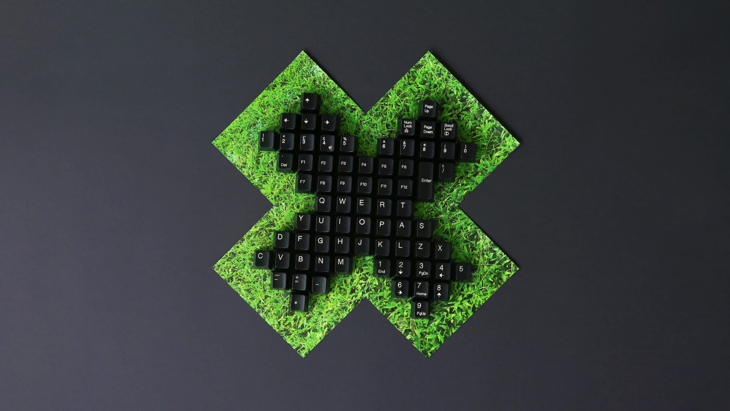An image of a keyboard shaped in an X design juxtaposed against a slightly larger X shape of grass